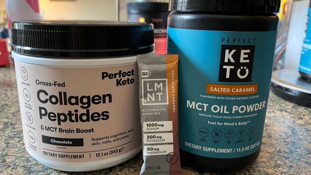 Tubs of Perfect Keto chocolate collagen powder and salted caramel MCT oil powder with a stick of LMNT chocolate caramel electrolyte powder.