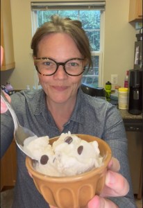 A smiling woman holds up a small bowl of chocolate chip keto ice cream.